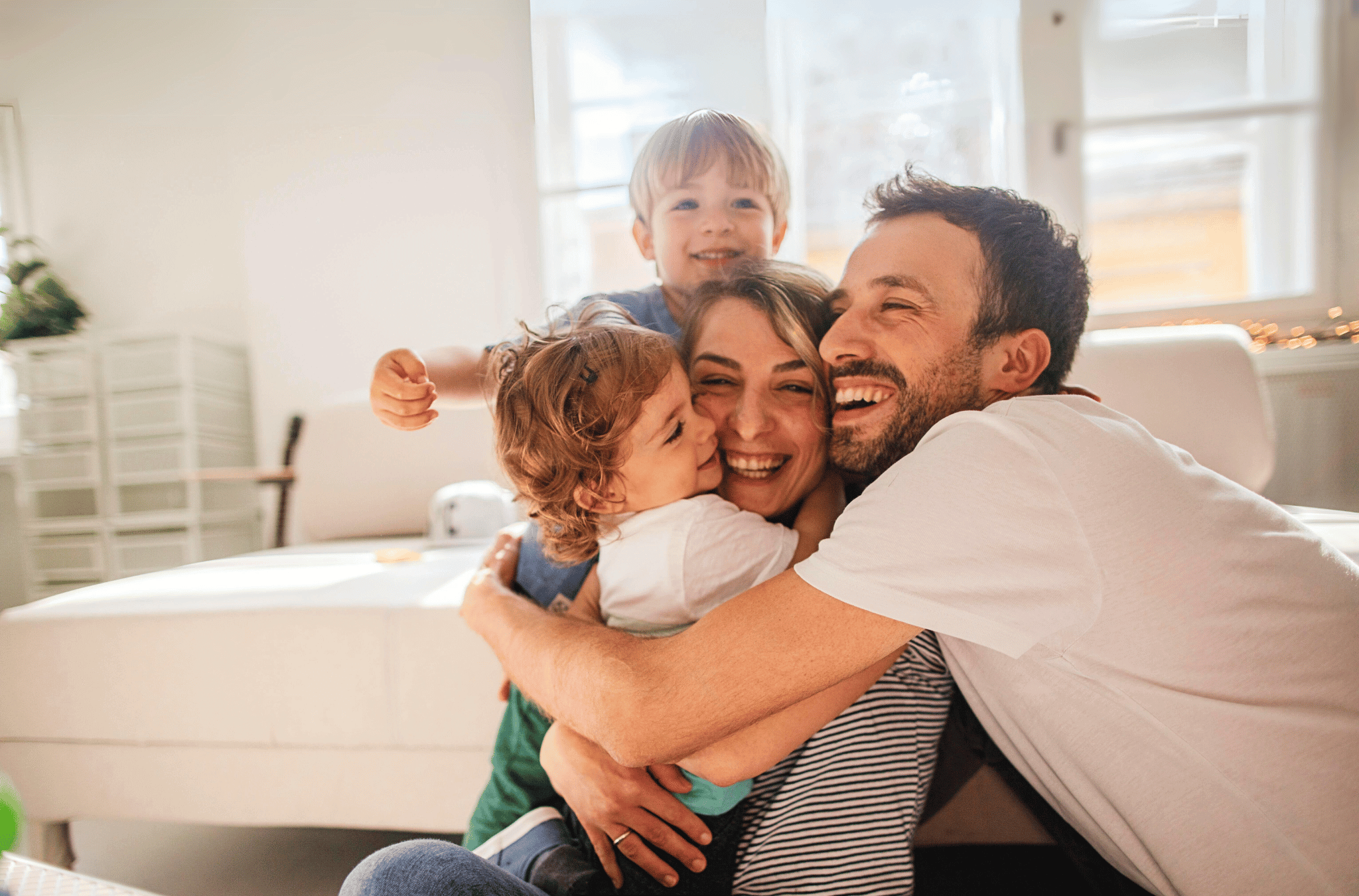 Happy family hug between two little boys, mom and father in living room